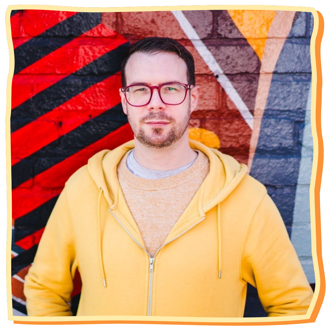Man wearing a yellow hoodie in front of a colorful geometric-patterned wall.